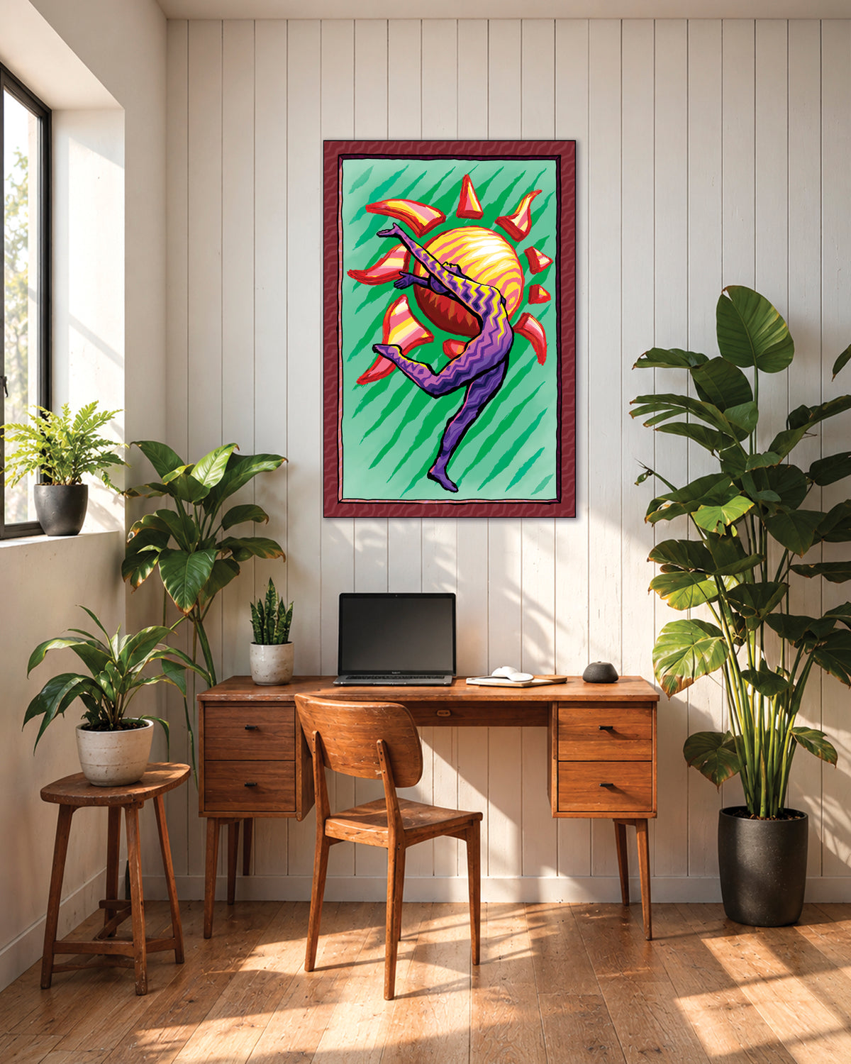 Sun Salutation art print above a wooden desk with a laptop, surrounded by houseplants in a sunny home office.
